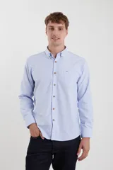 Camisa celeste de tejido texturado oxford, corte clásico, con cuello abotonado, mangas largas con puños ajustables, bolsillo en el pecho y cierre frontal con botones de madera.