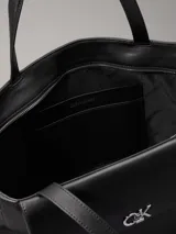 Cartera tote Calvin Klein color negro, confeccionada en piel sintética, con doble asa de hombro, cierre superior con cremallera, bolsillo externo con cierre giratorio y logo CK plateado.