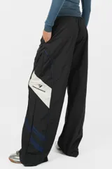 Pantalón deportivo gris de nylon, de calce recto y tiro medio, con elástico en la cintura, cordones ajustables y detalle de recorte con vivo a contratono en los laterales.
