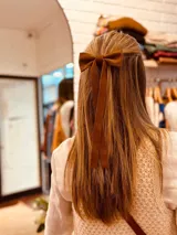 Moña de cuero color marrón con forma de lazo y tiras colgantes.