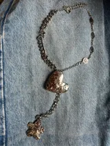 Collar metálico plateado con dije de corazón y de flor. La cadena está formada por dos modelos distintos: una con caritas sonrientes y otra de eslabones.
