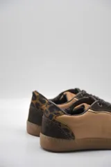 Zapatillas urbanas de cuero color beige con puntera y cordones marrones. Presentan un panel de animal print en el talón y suela de goma color caramelo.