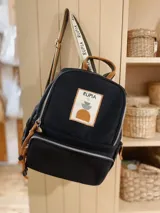 Mochila negra de nylon con grifa bordada, correas combinadas y detalles de cordones.