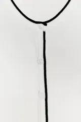 Chaqueta blanca de punto con cuello redondo y manga larga. Tiene vivos negros en el cuello, el borde frontal y los puños. Se cierra con botones en el frente.