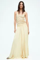 Pollera circular larga color amarillo pálido, de gasa transparente con viso corto. Presenta cintura alta con elástico, tiras finas largas en los laterales y bajo asimétrico con tajo pronunciado en los laterales.