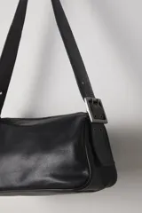 Bolso bandolera color crema, de cuero, con correa ancha ajustable con hebilla dorada.