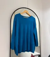 Sweater azul petróleo con cuello redondo, bolsillos delanteros y punto elástico en puños y bajo.