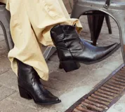 Bota de caña media baja realizada en cuero engrasado color negro, con detalle de punta fina y taco de 5 cm. El interior está forrado en forrería vacuna y el fondo es de madera.