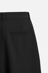 Pantalón negro de corte amplio, con pliegues en la parte delantera, bolsillos laterales y traseros de ojal.