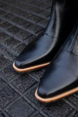 Bota corta de cuero negro con panel trasero de cuero vacuno blanco con manchas negras. Tiene cierre lateral y taco de madera.