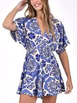 Monoprenda corta con estampado floral estilo azulejo en tonos azul y blanco. Presenta escote en V profundo, mangas cortas tipo mariposa y cintura ajustada con fruncido.