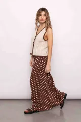 Chaleco tejido color crema con escote en V y ribete marrón. Presenta tres flores de crochet marrones a modo de cierre.