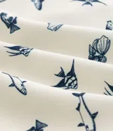 Bermuda de baño para hombre, color crema, con estampado repetitivo de peces azules. Presenta cintura elástica con cordón de ajuste y forro interior de malla.