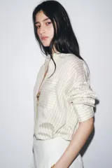 Camisa de manga larga con cuello solapa, a rayas verticales grises y blancas. Tiene un bolsillo de plastrón en el delantero y cierre frontal con botones.