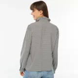 Camisa de manga larga con estampado vichy en blanco y negro, cuello alto con volantes y cierre frontal con botones.