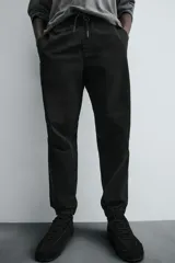 Pantalón jogger negro de corte slim fit, confeccionado en tejido de algodón con cintura elástica ajustable con cordón, bolsillos frontales y traseros de vivo, y bajo con puño elástico.