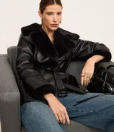 Blazer negro confeccionado en material sintético PU, con cuello y puños de piel sintética, cierre por cremallera y cinturón con hebilla en la cintura.
