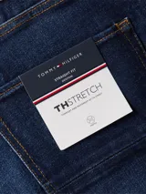 Jeans de corte recto color azul oscuro, con diseño de cinco bolsillos, cierre de botón y cremallera, cinta distintiva de Tommy Hilfiger sobre el bolsillo delantero y parche con logo en la parte posterior.