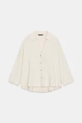 Camisa color crudo de cuello solapa y escote pico, manga larga amplia y bajo asimétrico. Cierre frontal con botones.