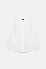 Camisa blanca amplia de cuello solapa y manga larga. Tiene un bolsillo de plastrón en el pecho, bajo asimétrico y cierre frontal con botones.
