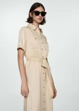Vestido camisero midi color beige, de tela satinada, con cuello camisero, mangas cortas, dos bolsillos de parche en el pecho, lazo ajustable en la cintura y cierre frontal con botones.