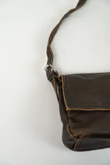 Cartera bandolera de cuero marrón oscuro con solapa y correa fina ajustable.