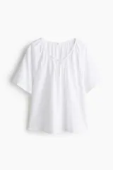 Blusa blanca de tejido liviano con mangas raglán cortas. Modelo de corte holgado con escote redondo levemente fruncido, abertura en V y tiras finas para atar adelante.