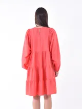 Vestido corto color coral, con cuello redondo, mangas abullonadas 3/4 y falda escalonada de tres niveles.