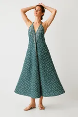 Mono largo de poliéster con estampado geométrico en tonos azul y blanco. Tiene breteles finos, escote halter pronunciado, corte ancho y cordón ajustable en la cintura.