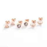 Set de tres pares de aros mini color oro rosa en acero quirúrgico: un par con forma de cubo con cristal, un par con forma circular y un par con forma de barra horizontal.