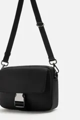 Bandolera negra de tela técnica con correa ajustable y extraíble. Tiene un compartimento principal con cierre de cremallera, un bolsillo interior con cremallera, un bolsillo frontal con solapa y hebilla de liberación rápida, y un monedero removible.