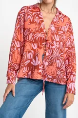 Blusa oversize de poliéster con estampado de animales y plantas en tonos rosa y marrón. Tiene cuello camisero, mangas largas y cierre frontal con lazos.