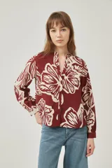 Camisa de poliéster con estampado floral en tonos borgoña y crema, corte holgado, cuello mao y cierre frontal con botones.