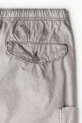 Pantalón cargo de algodón color gris claro, con corte holgado y cintura elástica ajustable con cordón. Presenta bolsillos cargo grandes en las piernas, pliegues cosidos en las rodillas y cordones ajustables en los bajos.