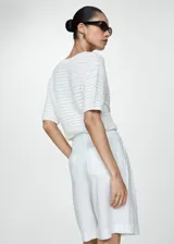 Short blanco de lino con tiro alto, corte recto, cinturón decorativo, bolsillos laterales y cierre oculto con botón, gancho y cremallera.