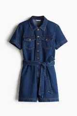 Mono corto de denim azul, con cuello camisero, cierre frontal con botones, mangas cortas, bolsillos superiores de parche con botón, bolsillos al bies y bolsillos insertados atrás. Incluye cinturón extraíble para atar en la cintura.