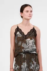 Top verde con estampado de figuras mitológicas en blanco y negro, escote en V con encaje negro y tirantes finos.
