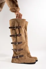 Botas altas color marrón claro, de cuero gamuzado, con caña alta y múltiples correas horizontales con hebillas metálicas.