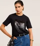Remera negra de algodón con corte slim, cuello redondo y mangas cortas. Presenta un bloque rectangular frontal con lentejuelas plateadas.