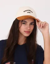 Gorra de béisbol color beige con visera marrón, bordado frontal con la inscripción "Wednesday 1996" y regulador metálico trasero.
