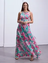 Vestido largo de gasa estampada con flores rosas y turquesas sobre fondo blanco. Tiene escote halter con ojal, cintura fruncida y falda con sobrecapa.