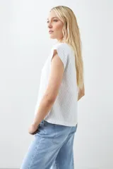 Remera blanca de corte holgado con cuello en V y mangas cortas. Presenta detalle de tela a rayas verticales en los laterales con botones decorativos.