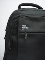 Mochila negra con logo Forum Industries Co. estampado en blanco. Cuenta con múltiples compartimentos con cierre, dos bolsillos laterales de red y asa de mano acolchada.