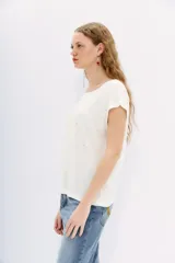 Remera de lino color crudo con cuello en V y mangas cortas. Tiene tachas plateadas termofijadas en el frente.