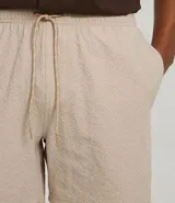 Bermuda de microfibra color beige, con cintura elástica y cordón ajustable. Presenta textura en el tejido y un bolsillo lateral.