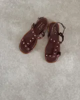 Sandalias chatas de cuero vacuno color marrón con tiras con apliques de tachas doradas.