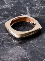 Pulsera rígida dorada con forma cuadrada y cierre a presión.
