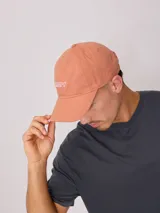 Gorra de lona color salmón con logo de la marca bordado en blanco.