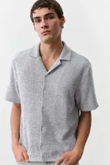 Camisa de manga corta color gris claro, de punto con textura de mezcla de algodón. Modelo con cuello abierto, tapeta lisa y bajo recto. Corte estándar para una silueta clásica y cómoda.