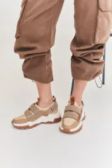 Zapatillas deportivas con diseño moderno en tonos blancos y dorados, con cierre de velcro para mayor comodidad.